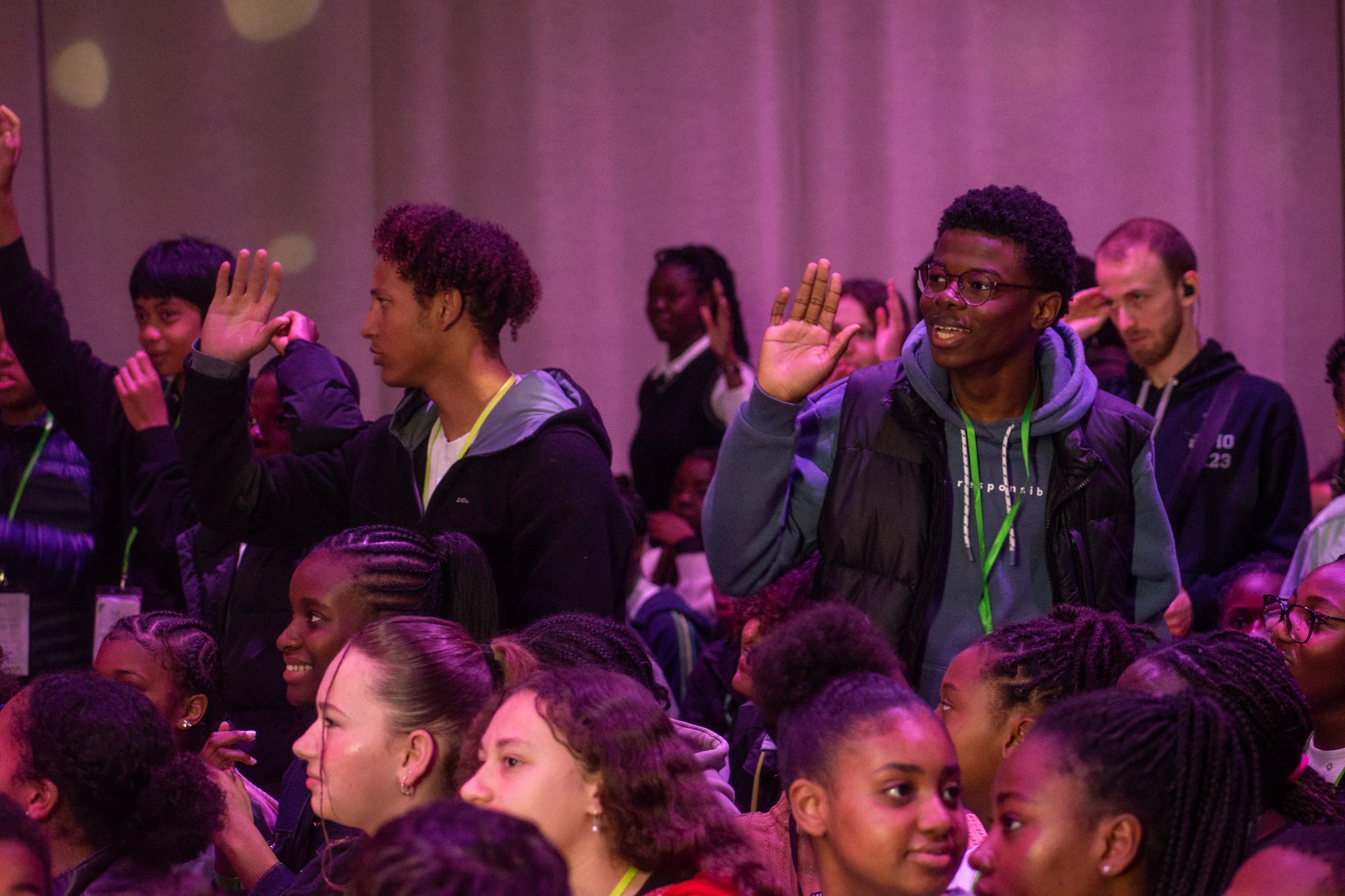 Des jeunes lèvent la main pendant un temps de louange, sous une lumière rose