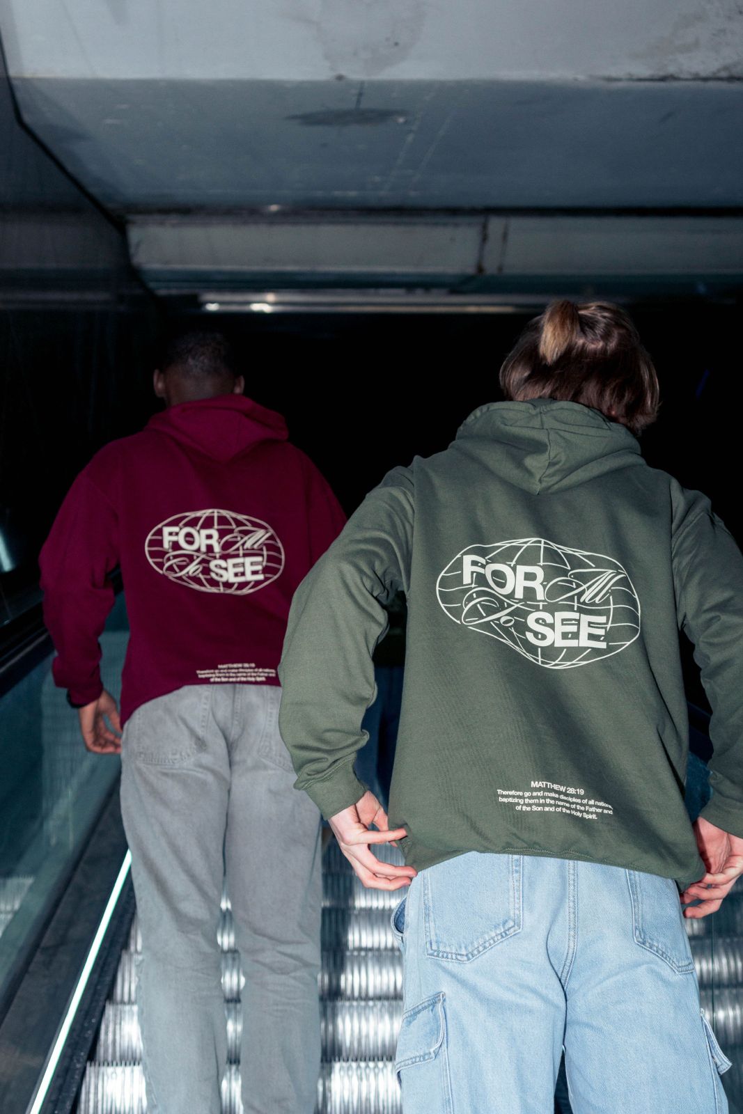 Deux sweats PAJE « For all to see », vus de dos dans un escalator